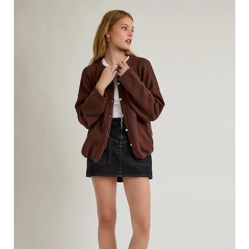 front view of the model wearing a brown cardigan. shows the button down closure. also shows the black denim skirt she is wearing on a beige background.