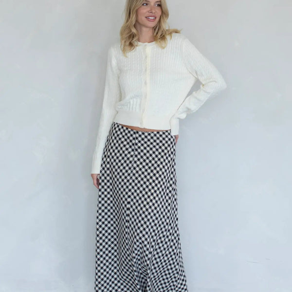 Woman wearing a white cropped jacket and black and white checkered skirt against a plain background
