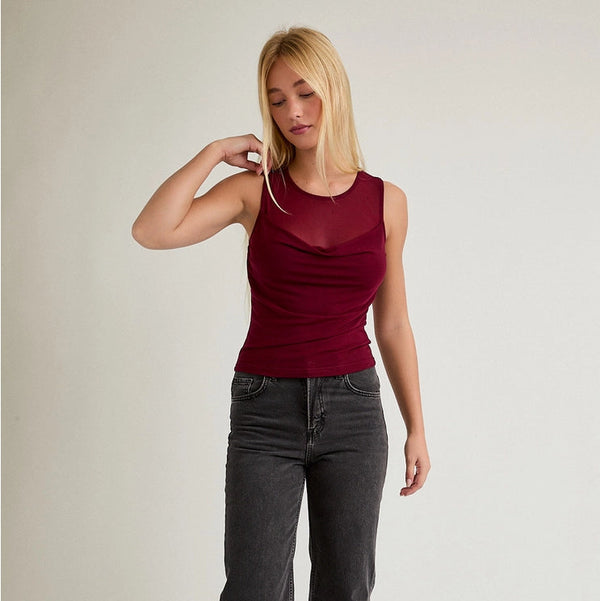 Woman wearing a red sleeveless top and dark jeans on a plain background