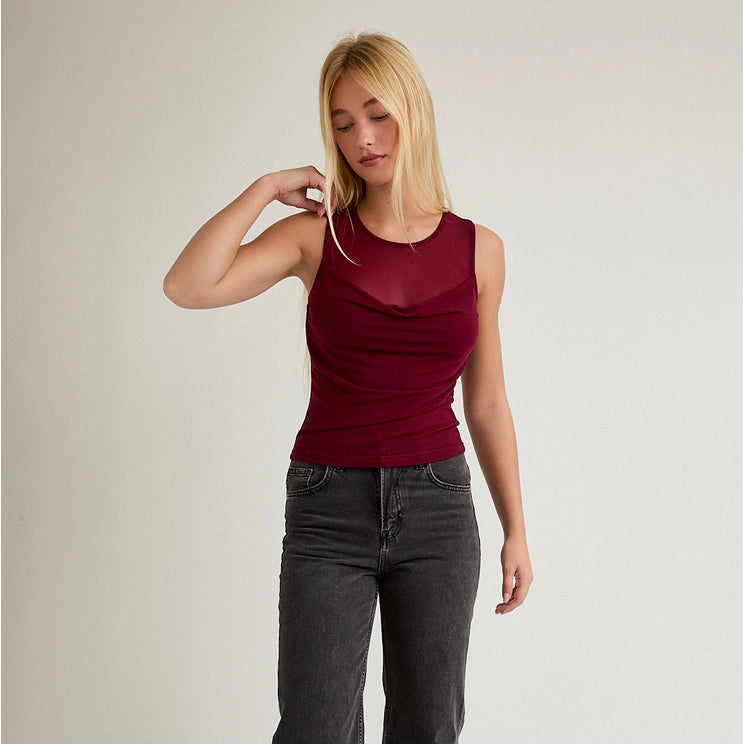 Woman wearing a red sleeveless top and dark jeans on a plain background