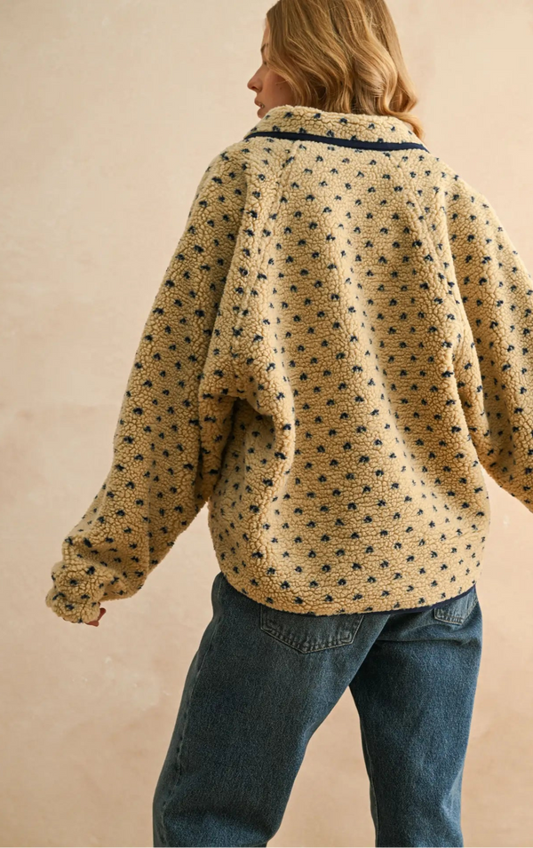 Person wearing a patterned beige shirt and blue jeans against a beige background