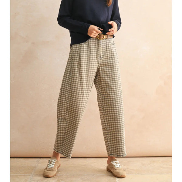 Woman wearing a navy sweater and plaid pants against a beige background