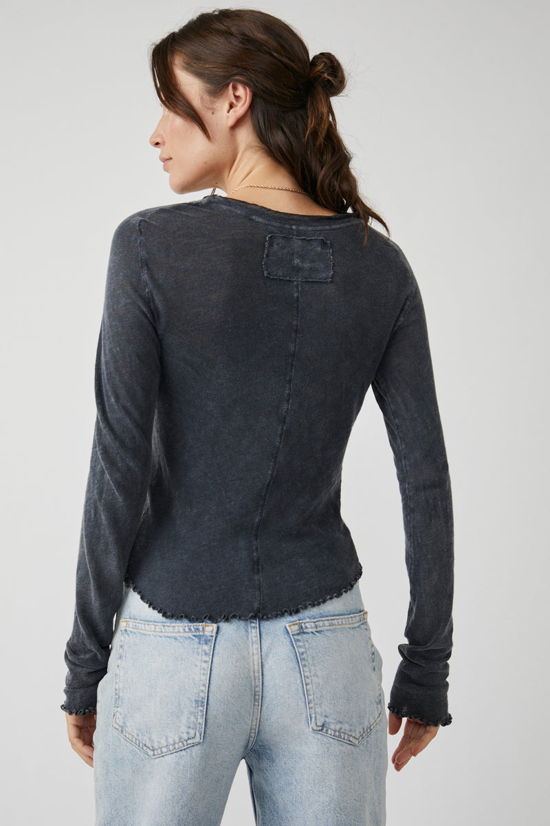 back view of the model wearing the be my baby long sleeve in black. shows the lettuce style trim on the hemline and the cuffs. also shows the scoop neckline, the rounded bottom hem and the defined seaming down the middle.