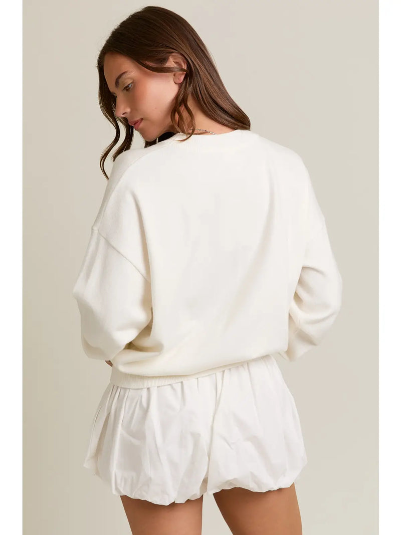 back view of the model wearing the puppy long sleeve sweater. shows the dropped shoulders. also shows the white color, the tighter band and the oversized fit. 