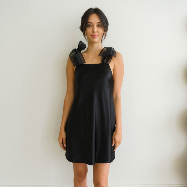 Front view of model wearing the Kate Mini Dress. Shows the mini dress with the square neckline. Also shows the exaggerated bow tie straps. 