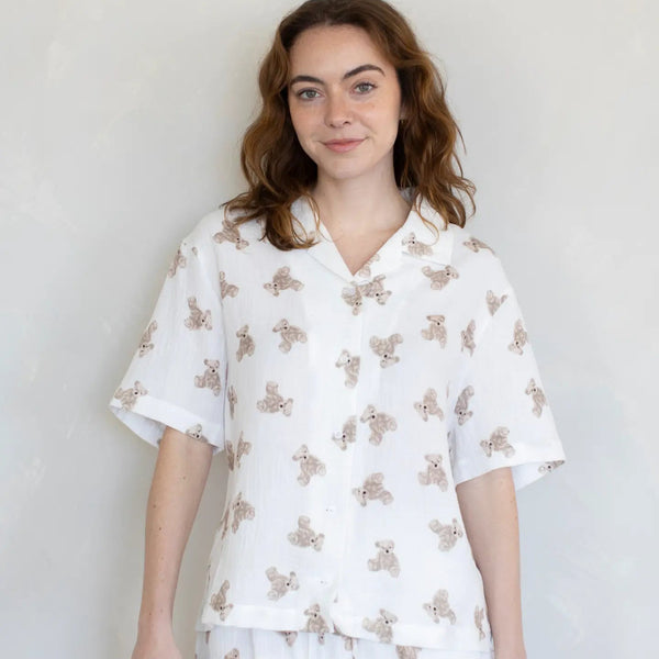 Woman wearing a white pajama set with a teddy bear pattern on a plain background