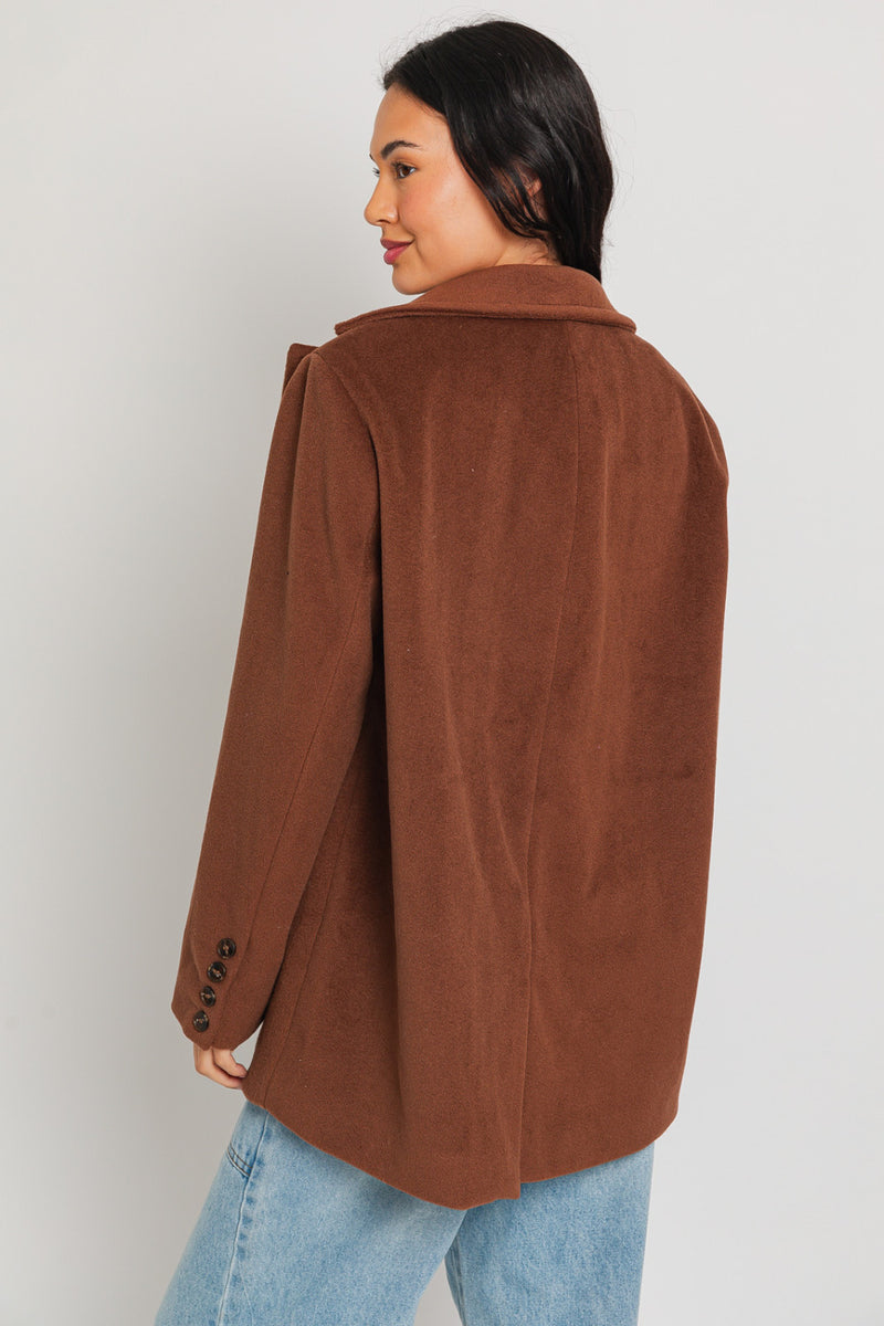Back view of model wearing blazer coat. Shows the 4 buttons on the cuffs. Also shows the oversized fit and the beautiful brown color. 