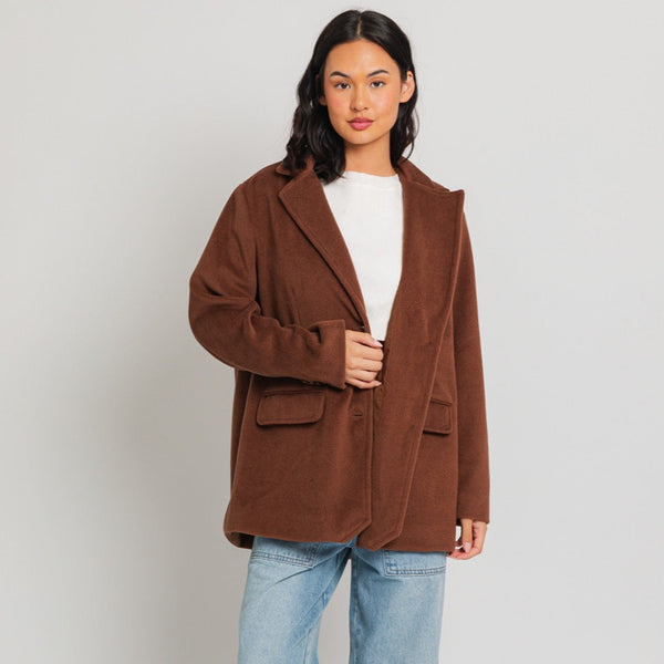 Front view of model wearing blazer coat. Shows the front pockets, the collar, the button closure and the beautiful color brown. 