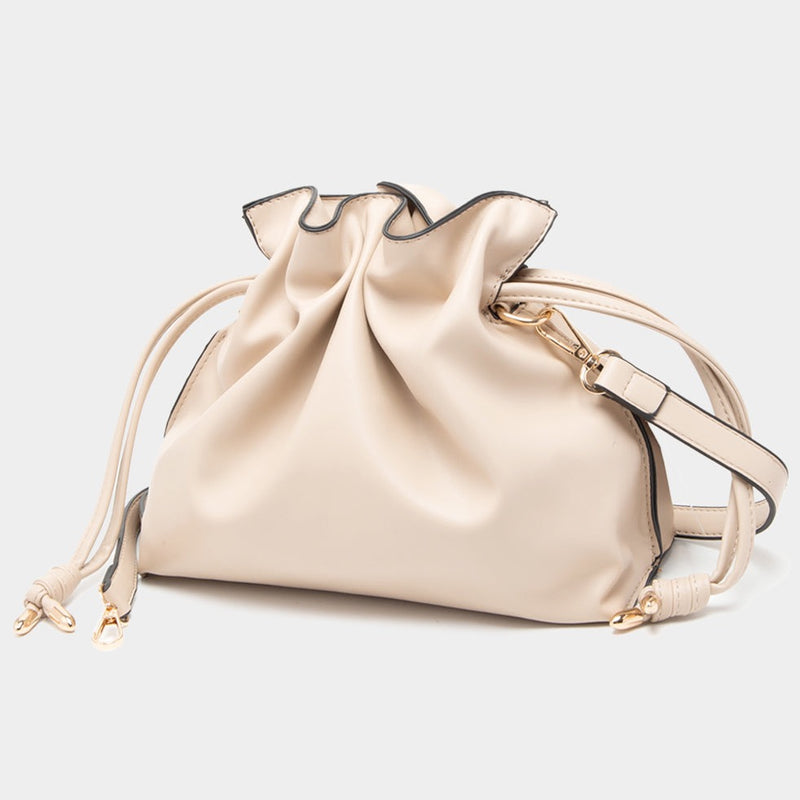 Front view of bucket bag. Shows the drawstring closure. Also shows the adjustable and detachable strap, the gold hardware and the beige color.