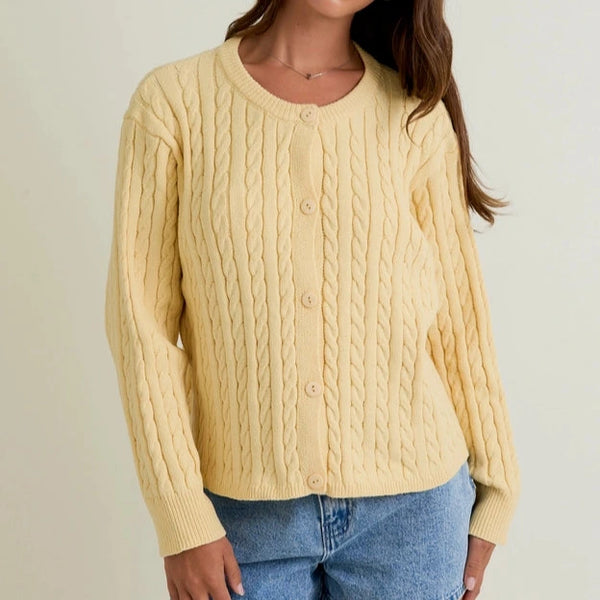 Woman wearing a yellow cable knit sweater and denim shorts on a plain background