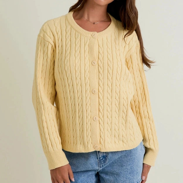 Woman wearing a yellow cable knit sweater and denim shorts on a plain background