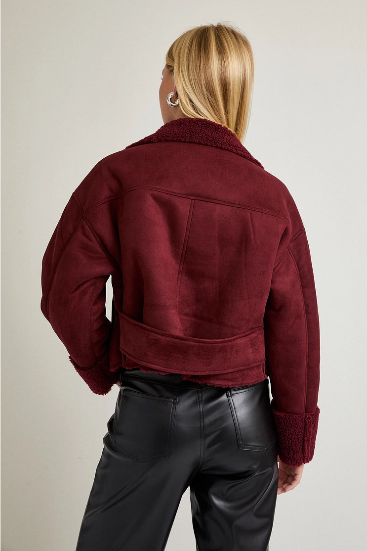 Person wearing a burgundy jacket and black pants on a plain background