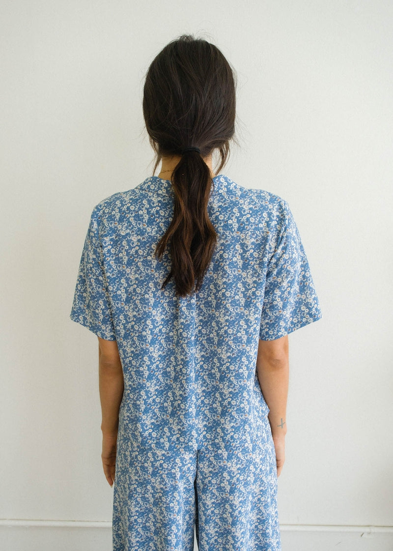 Back view of model in Selena floral button down. Shows the back of the collar and of the shoer sleeves. Also shows the pleating in the middle of the top as well. 