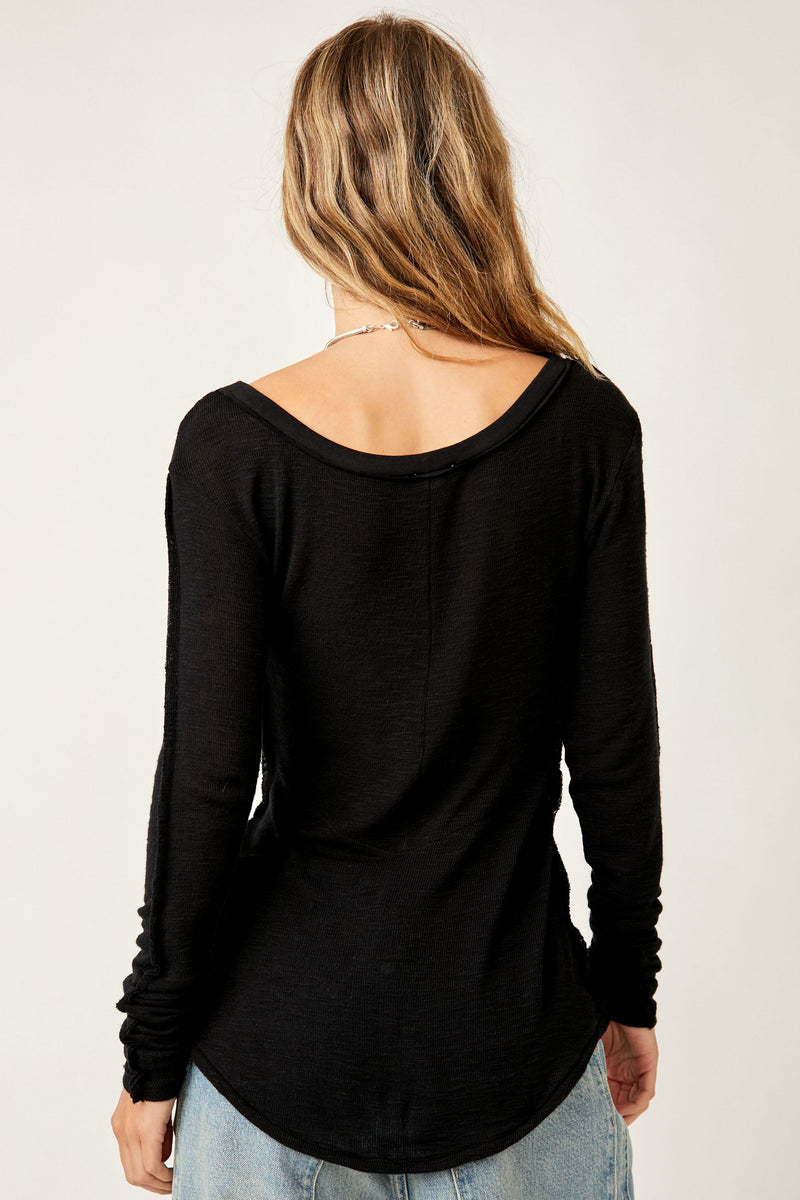 back view of model wearing the cabin fever layering top in black. shows the back scoop neckline. also shows the shirttail bottom hem, the sheer fabric, and the fitted sleeves. 