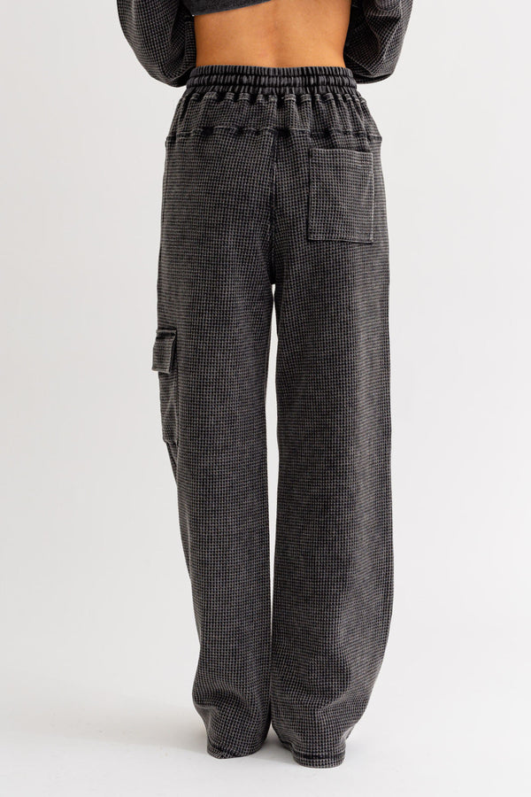 Back view of model wearing cargos. Shows the one back pocket. Also shows the defined seam across the rear, the waffle knit matieral, the wide leg and the charcoal color. 