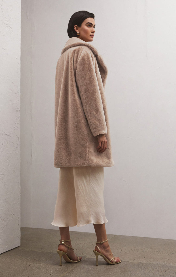 back/ side view of the model wearing the jewel fur coat in chai. shows the notch collar. also shows the faux fur detail, the mid length and the defined seaming throughout. 
