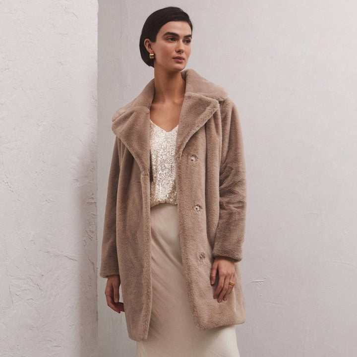 front view of the model wearing the jewel fur coat in chai. shows the notch collar. also shows the snap button closure, the two front pockets, and the relaxed fit.