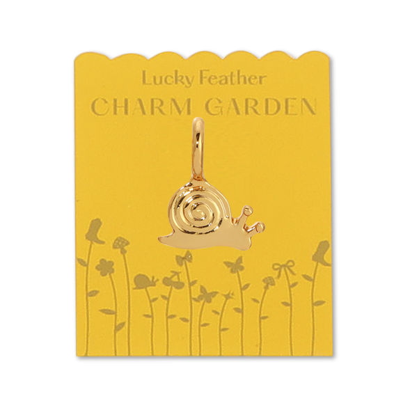 Front view of snail charm on yellow packaging. Shows the gold snail charm and the gold flowers and writing lucky feather charm garden on yellow packaging. Charm is a little smaller than a dime. 