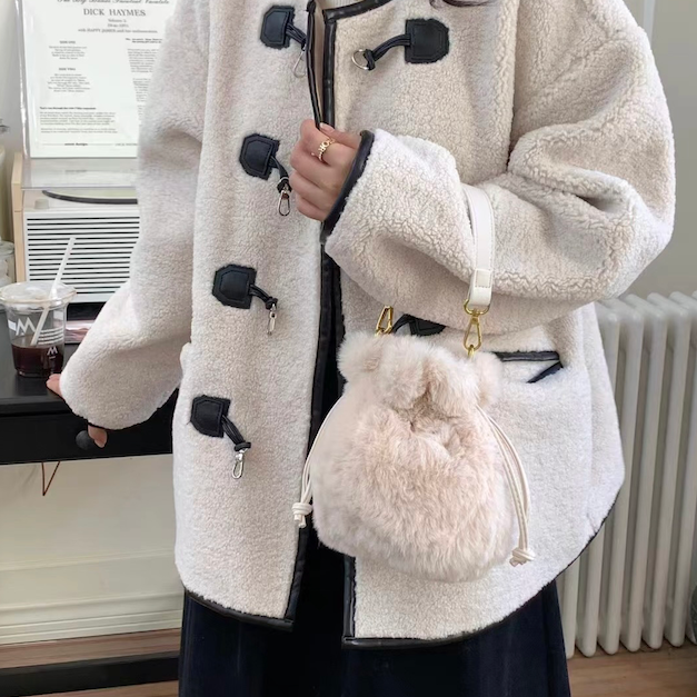 front/side view of model wearing daphne fur bucket crossbody in cream. shows the shoulder strap. also shows the gold hardware, the two pull closures and the faux fur body. 