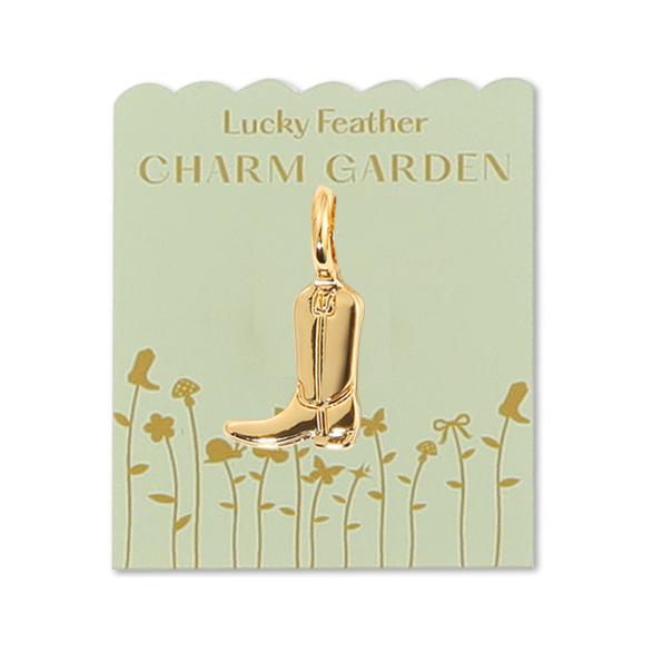 Front view of cowboy charm on packaging. The packaging is a light green with gold words 'LUCKY FEATHER CHARM GARDEN" and gold flowers. Also in the middle shows the gold cowboy charm. 