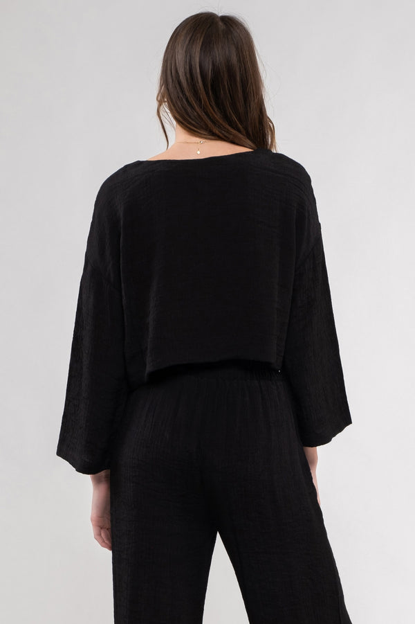 back view of the model wearing the Vivian cropped top in black. shows the drop shoulders. also shows the wide U neckline, the wide sleeves and the boxy, relaxed fit. 