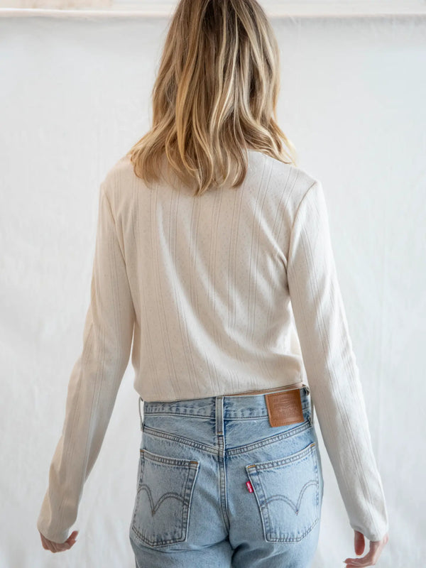 Person wearing a beige long-sleeve top and light blue jeans against a white background