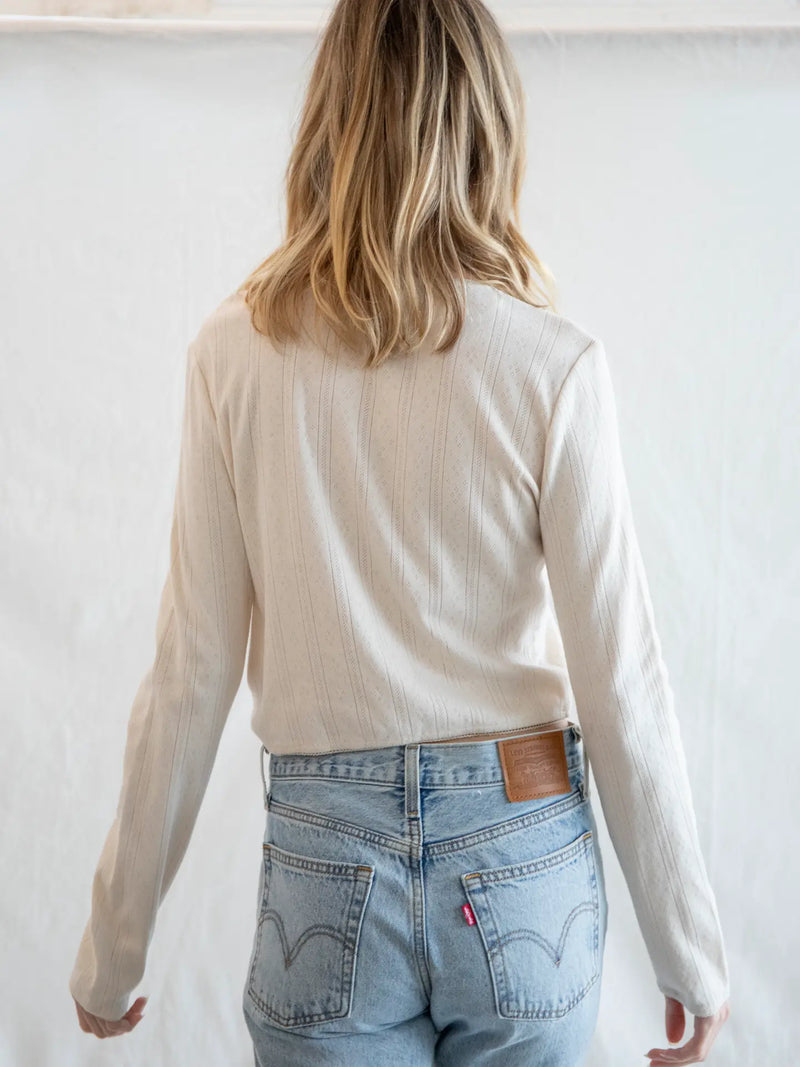 Person wearing a beige long-sleeve top and light blue jeans against a white background