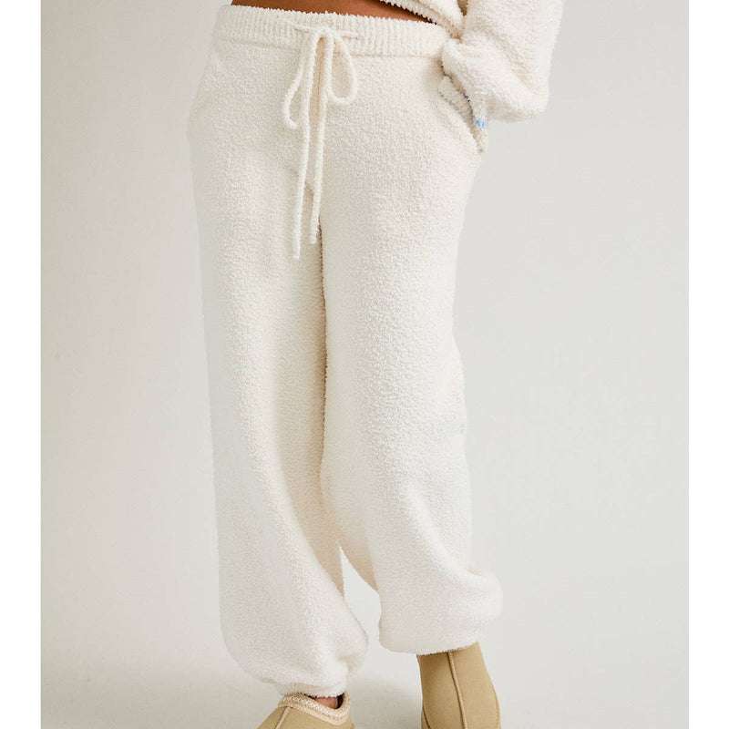 Person wearing cream-colored fleece jogger pants and beige slip-on shoes on a light gray background