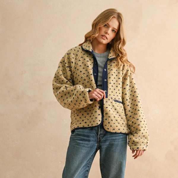 Woman wearing a patterned jacket, denim jeans, and white sneakers against a beige background