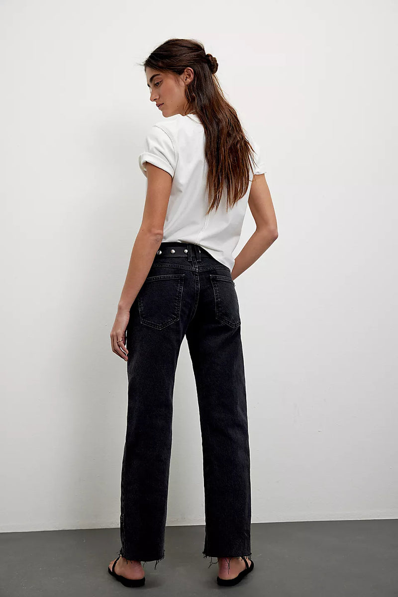 back view of the model wearing the rise taker jeans. shows the raw hem. also shows the back pockets, the mid-rise, the color of the pants that is black and the mid -rise.