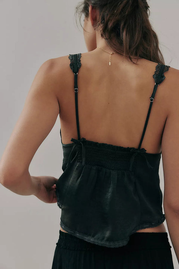 back view of the model wearing the tell me more cami in black. shows the bow detail on the back straps. also shows the adjustable straps, the lace detailing and the semi cropped. 