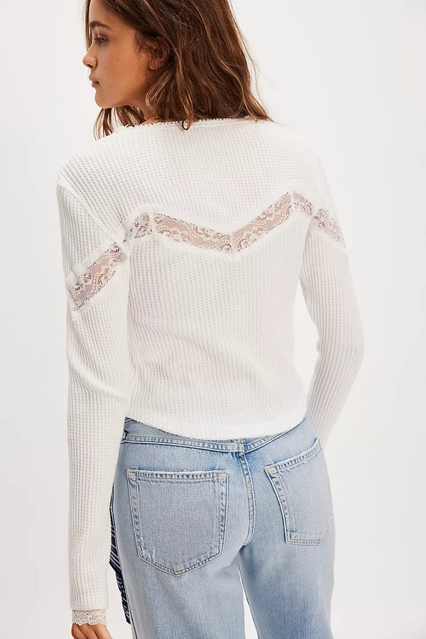Woman wearing a white ribbed sweater with lace details and light blue jeans on a white background