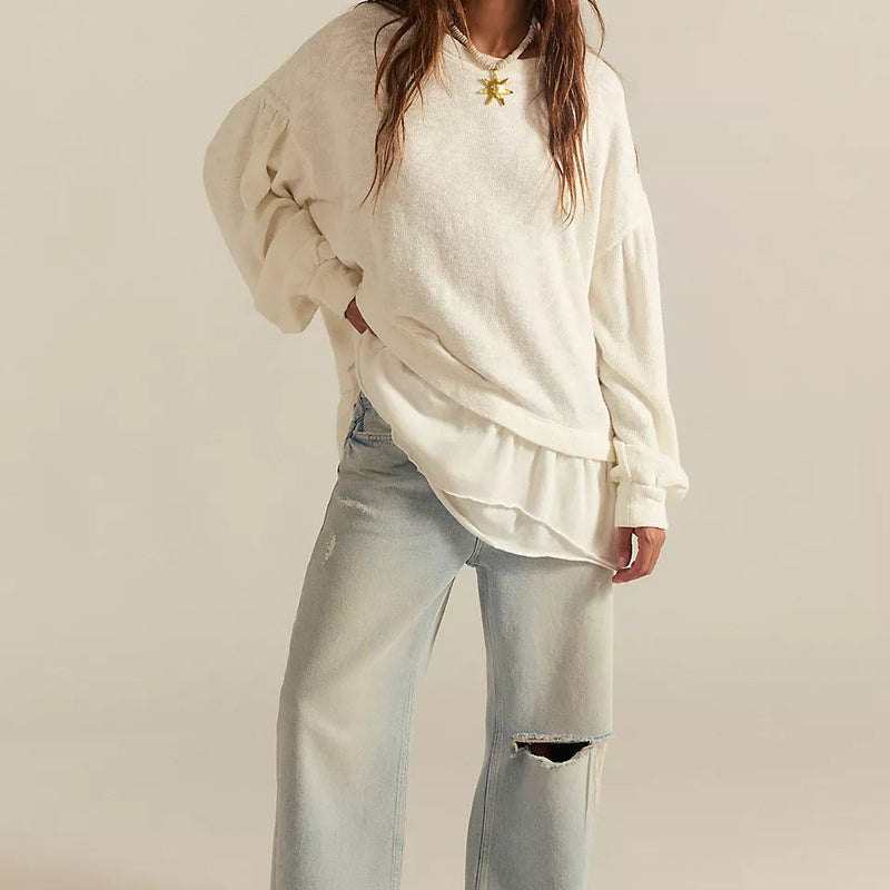 Woman wearing a light-colored oversized sweatshirt and light blue jeans on a beige background