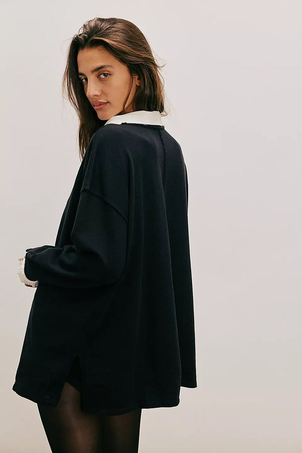 Person wearing a black oversized sweater with a white collar against a plain background