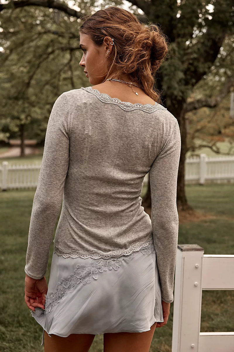 Woman wearing a gray long-sleeve top and light gray skirt in an outdoor setting.