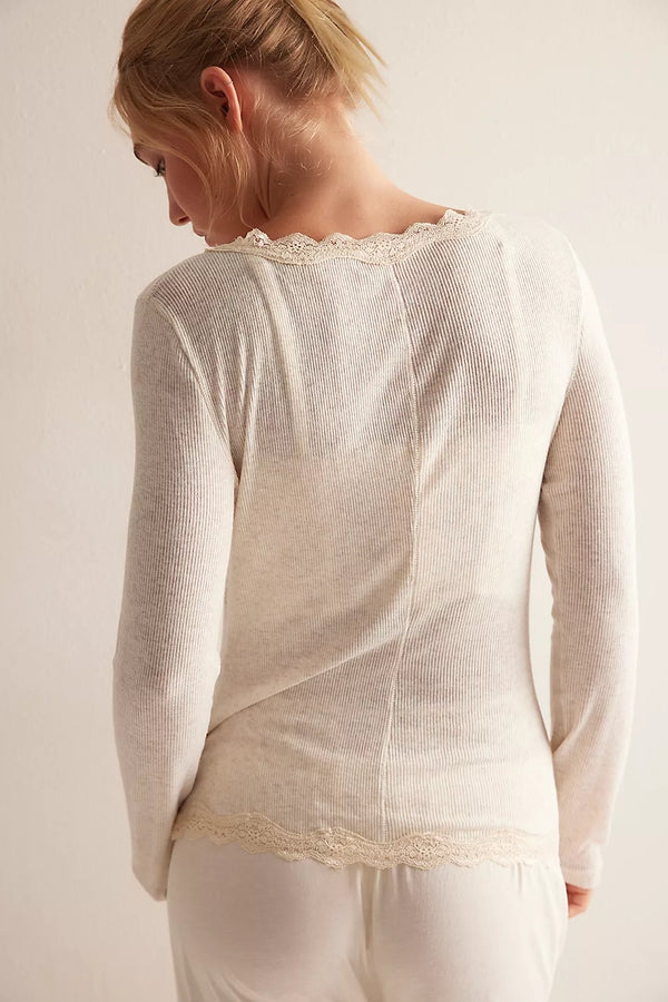 Woman wearing a cream-colored long-sleeve top with lace trim on a plain background