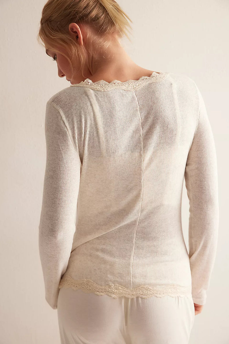 Woman wearing a cream-colored long-sleeve top with lace trim on a plain background