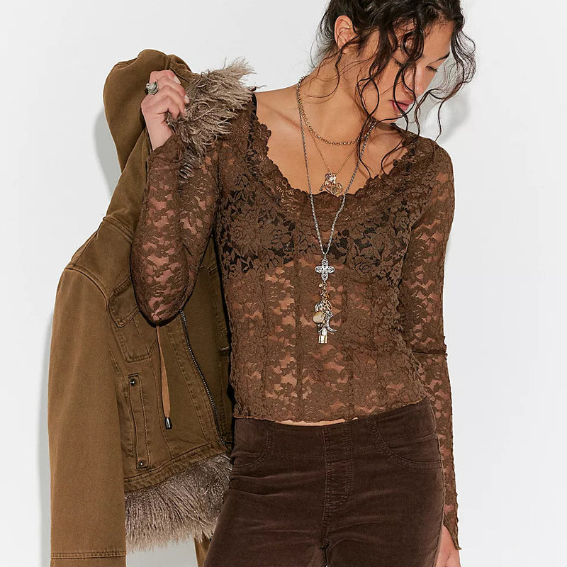 Woman wearing a brown lace top and velvet pants holding a brown jacket against a white background