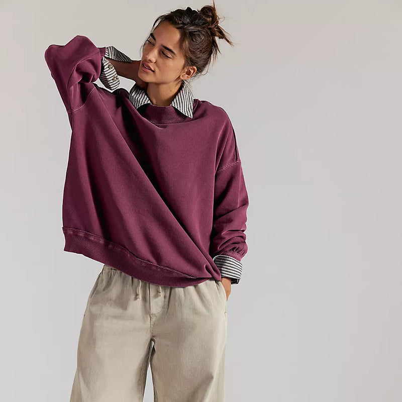 Person wearing a burgundy oversized sweater and beige pants on a plain background
