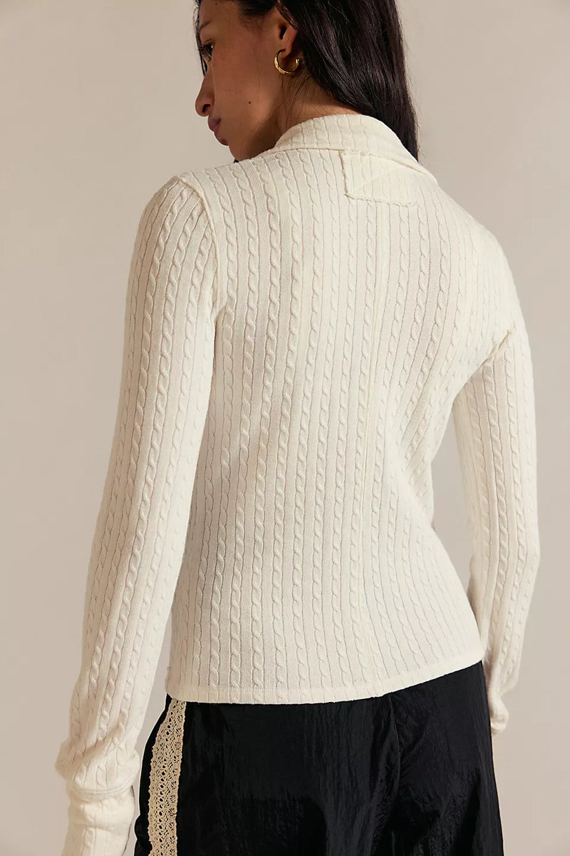 Person wearing a cream cable knit sweater against a neutral background