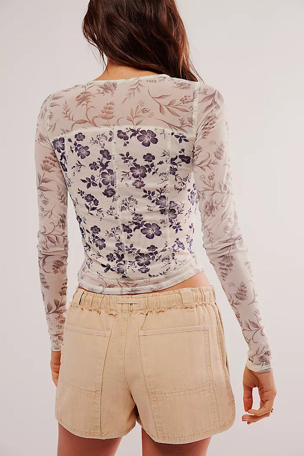 back view of the model wearing the bettys garden top. shows the sheer sleeves. also shows the exposed seaming, the fitted style and the floral design. 