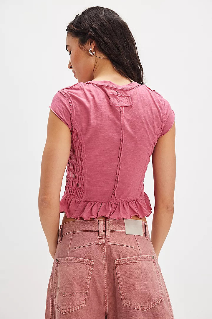 back view of the model wearing the sylvie tee. shows the exposed seaming. also shows the ruffle bottom, the cap sleeves and this pink/rose color. 