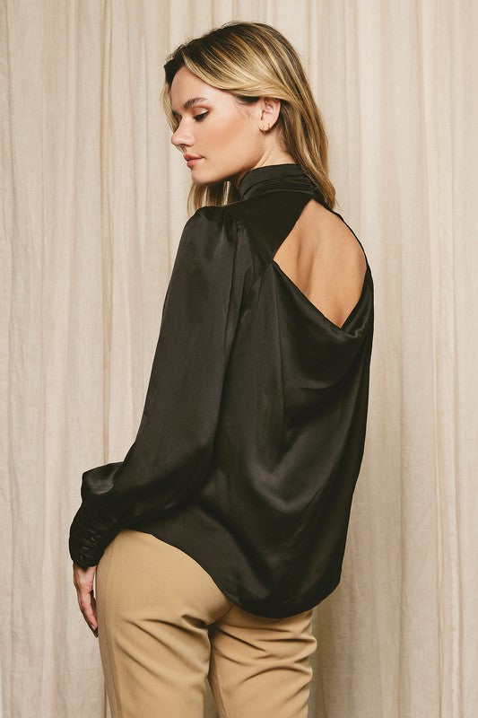 Back/side view of the model wearing blouse. Shows the cutout back detail. Also shows the back is little longer than front and  the button details on the cuffs. 