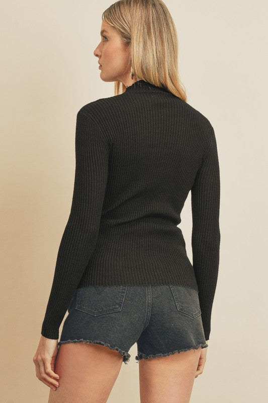 Back view of model wearing sweater. Shows the mock neck. Also shows the long sleeves, ribbed detail and the long sleeves. 