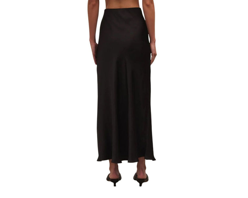 back view of model wearing europa poly sheen skirt in black. shows the midi length. Also shows the lettuce trim at the bottom of he skirt.