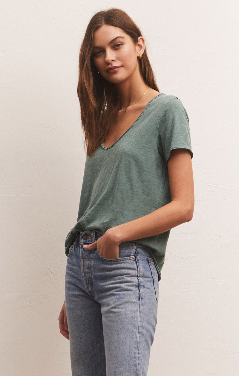 shows angled view of model in green t shirt. shows the low scoop neckline and looser fit.
