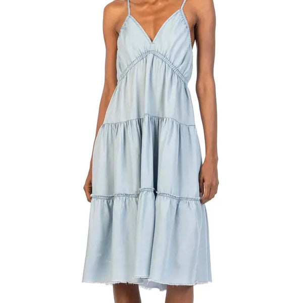 Front view of knee length, chambray dress. Features v-neckline with elastic under bust. Tiered skirt with raw hemline.