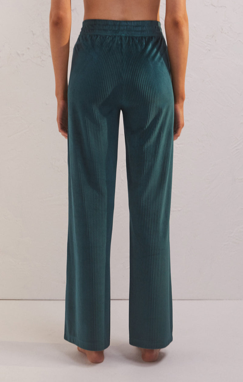Back view of model wearing pants. Shows the stretchy waistband. Also shows the high waist, the ribbed detail, the flare bottoms and the rich pine color.