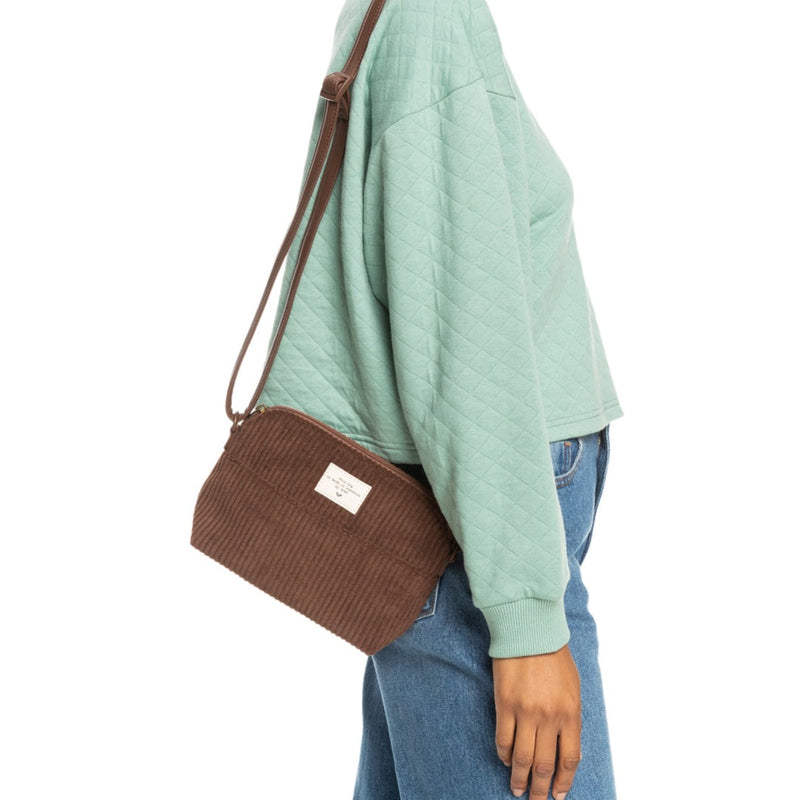shows model wearing crossbody bag. here you can see the corduroy fabrication, top zipper, and adjustable strap.