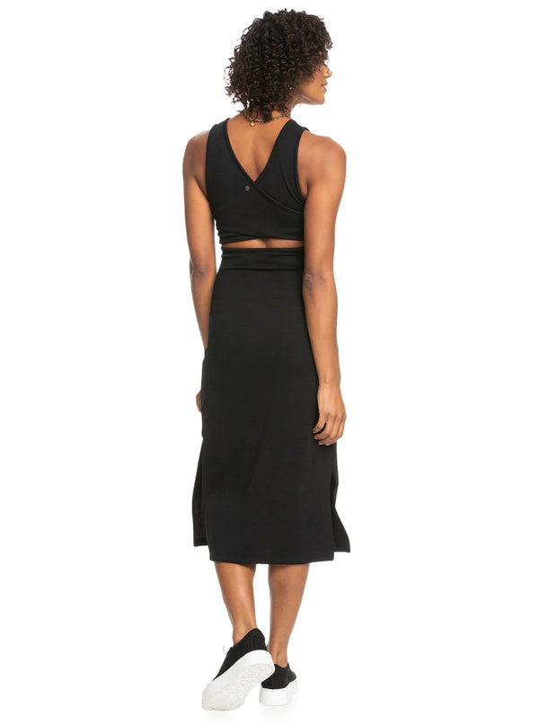 back view of the model wearing the good keepsake midi dress in black. shows the back v neckline. also shows the back slit, and the midi length. 